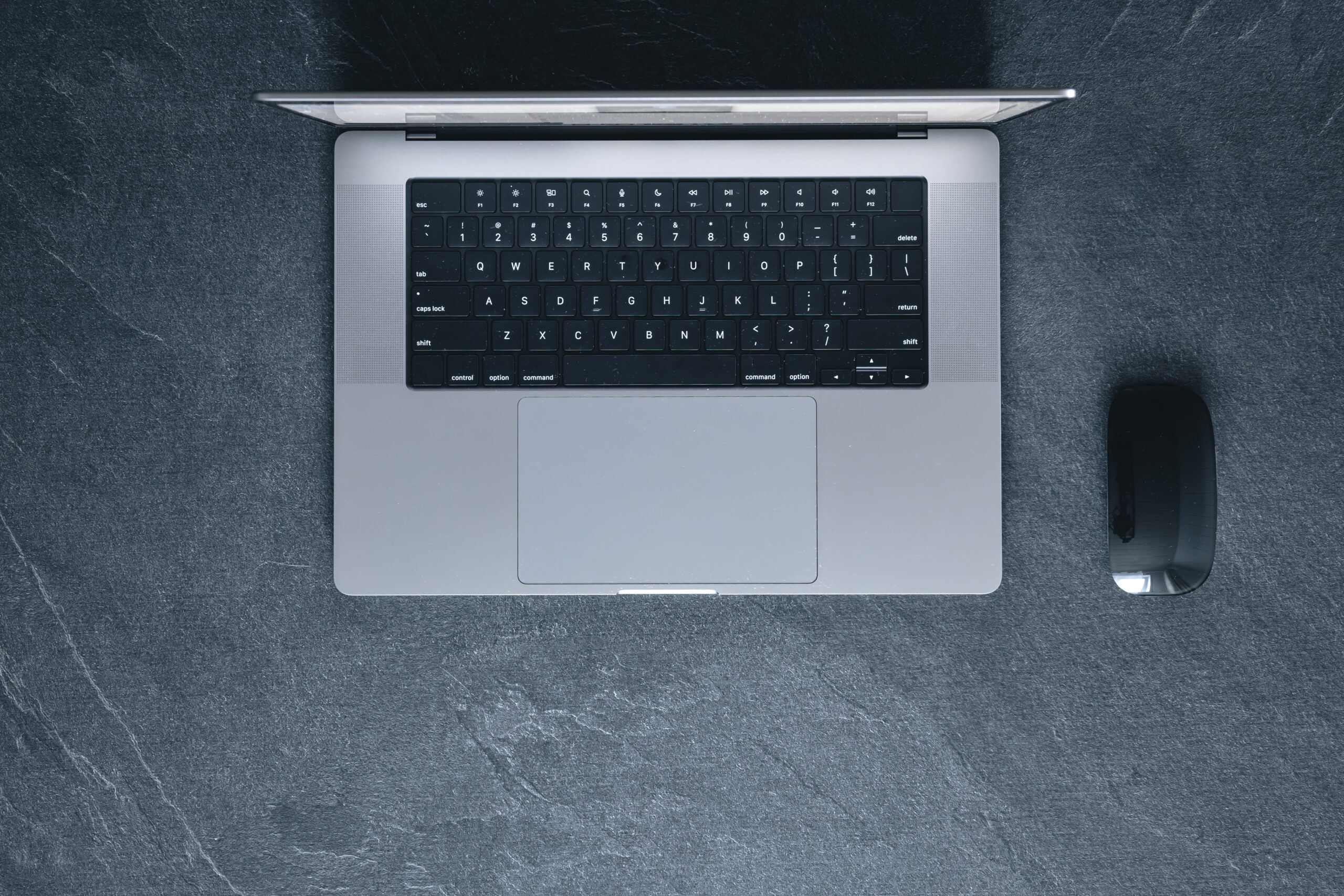 laptop and computer mouse on a dark textured background, top view.